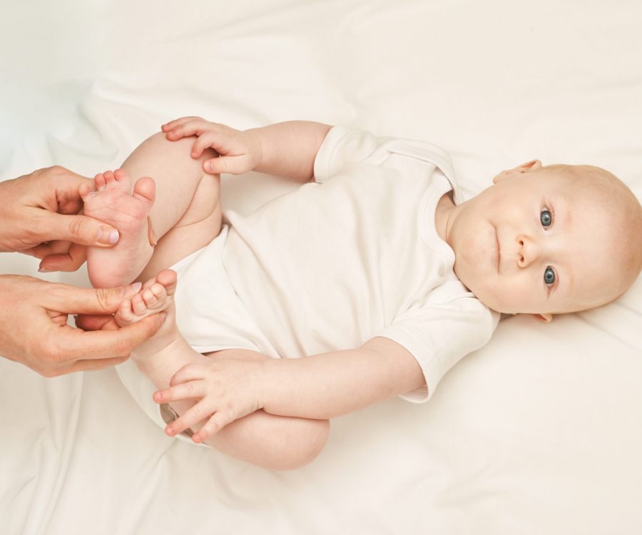 Cute small boy lying at bed. Childhood concept. Light background. Serious child. Copyspace. Stay home. Onesie mockup. Foot massage. White clothes
